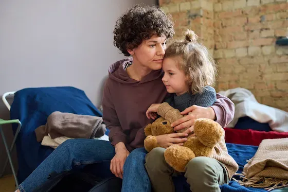 A mother and her child sitting together with a teddy bear in a shelter setting